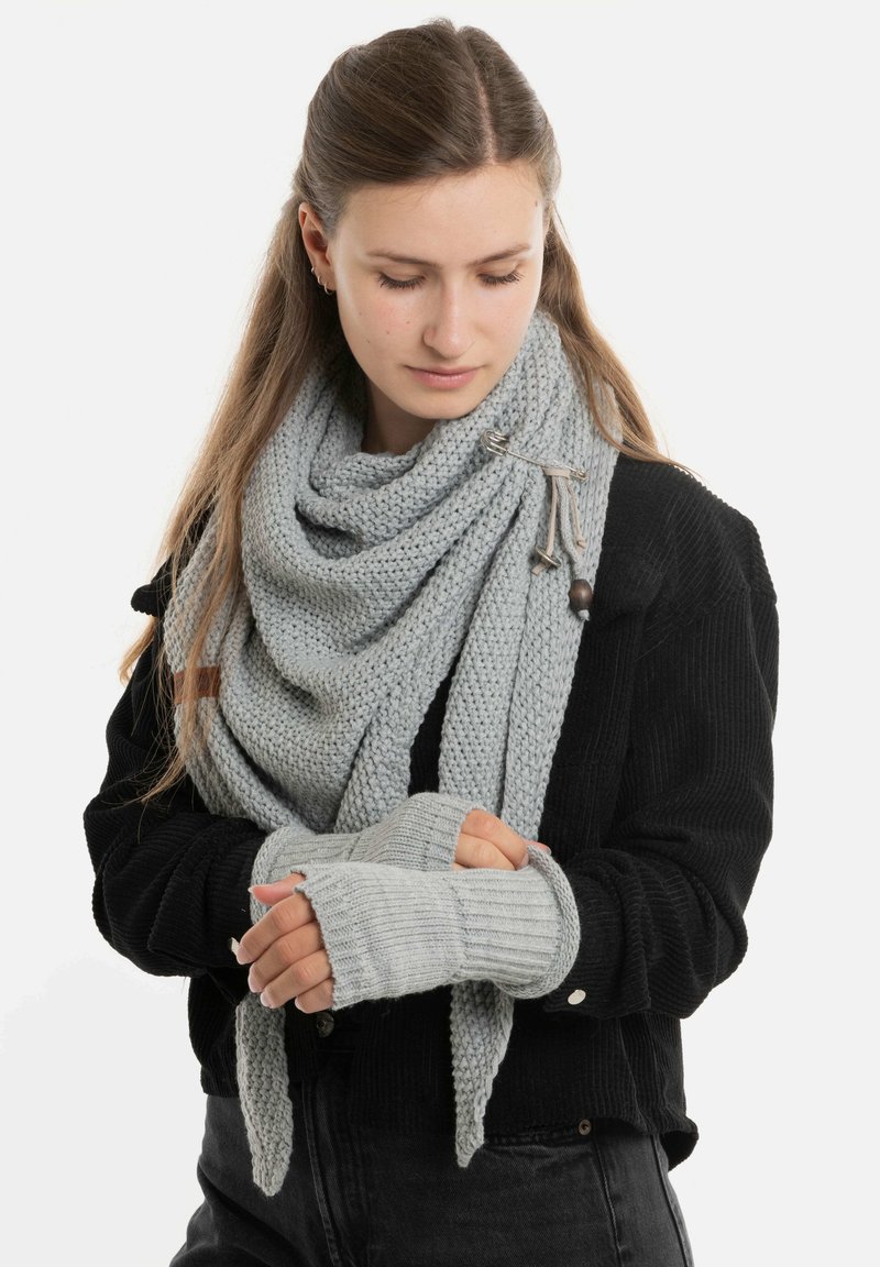 Lichtgrijze gebreide sjaal draped om de nek met bijpassende vingerloze handschoenen. De sjaal heeft een gestructureerd patroon en een houten accent.