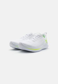 Baskets de sport blanches avec un dessus en mesh respirant, des détails texturés et des accents verts néon sur la semelle et le logo. Design léger.