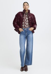 Bordeaux puffjakke med blank finish, mønstret langærmet bluse, høj midje blå jeans og brune ankelstøvler.