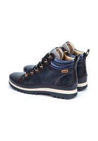 Bottes ankle en cuir bleu foncé avec des accents gris clair, des éléments en or et une semelle texturée. Dotées d'un col rembourré et d'une languette à l'arrière.