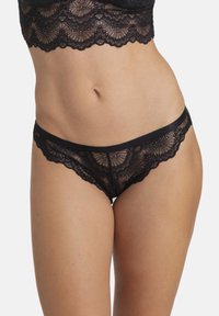 Črn čipkast thong z valovitimi robovi, ki vsebuje zapletene cvetlične vzorce in gladko pasnico. Polprosojna tekstura izboljšuje dizajn.
