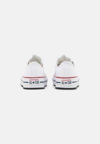 Zapatillas de lona blancas con un diseño de caña baja, acentos en rojo y azul, suela de goma y la marca "CONVERSE ALL STAR" en el talón.
