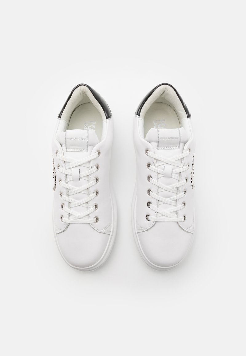 Baskets blanches avec une tige en cuir lisse, des accents noirs sur le talon, et un design classique à lacets doté d'œillets en argent et de détails de logo.