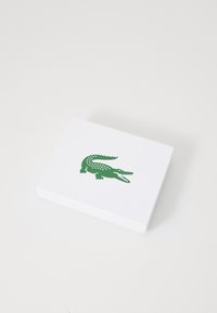 Bloc-notes bianco con finitura testurizzata, con un logo di coccodrillo verde stampato sulla parte anteriore. Forma rettangolare.