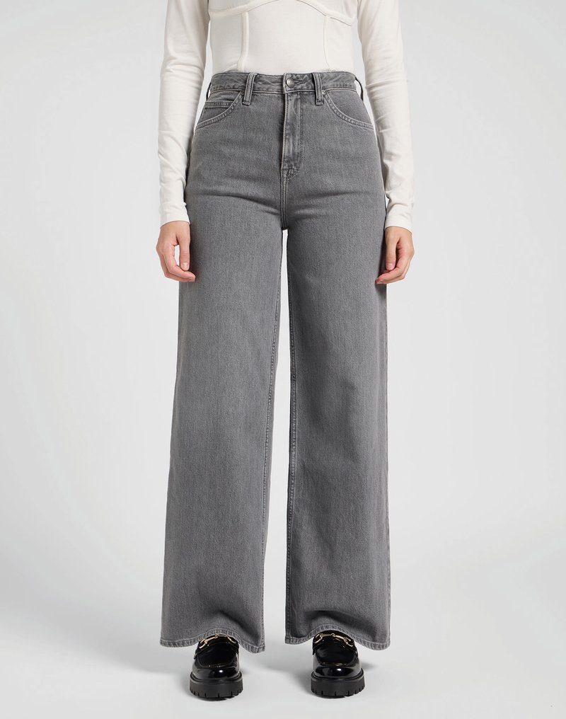 Jeans de pierna ancha en gris, confeccionados en denim, con cintura alta, bolsillos frontales y un dobladillo limpio. Combinados con zapatos de plataforma negros y gruesos.