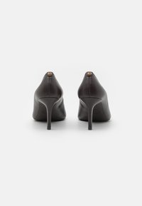 Des chaussures à talons hauts en cuir noir avec un design à bout pointu, présentant une silhouette minimaliste et un petit accent de logo doré au niveau du talon.