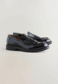 Black patent leather loafers with a smooth finish, featuring a decorative fringe, a low block heel, and stitching details along the seams.