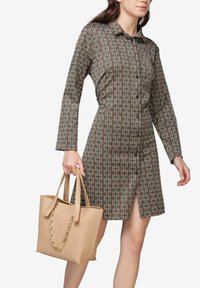 Knapp-up kjole med et geometrisk mønster i brune og cremede farver, lange ærmer og en slidse til låret; parret med en beige tote taske med kæde detaljer.