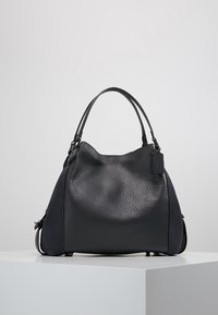 Czarna skórzana torebka o fakturowanej powierzchni, wyposażona w krótkie uchwyty, o zaokrąglonym kształcie oraz z delikatną metką z logo z boku.