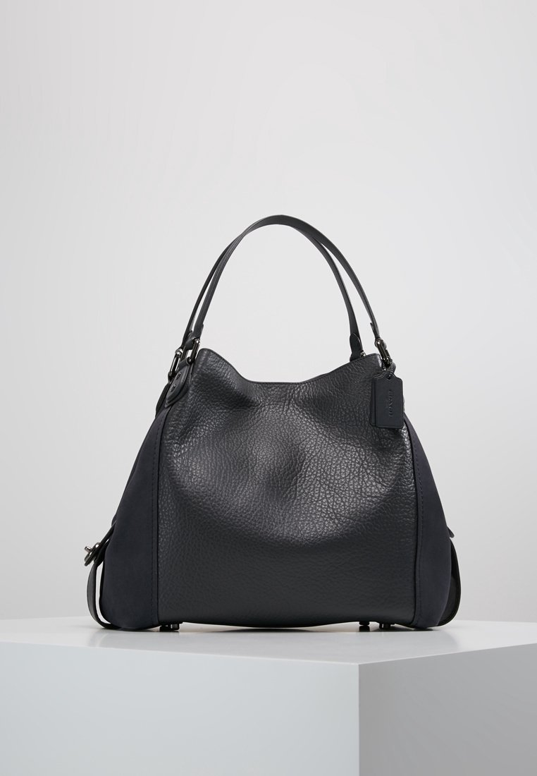 Czarna skórzana torebka o fakturowanej powierzchni, wyposażona w krótkie uchwyty, o zaokrąglonym kształcie oraz z delikatną metką z logo z boku.