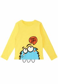 Gelbes Langarmshirt mit einem blauen Monster-Graphic, das große Augen hat und einer Sprechblase "WAS GIBT'S?" in Orange. Aus weichem Baumwollmaterial.