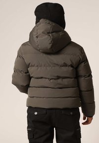 Doudoune verte olive avec des coutures horizontales, capuche fixée et col côtelé. Portée sur un pantalon cargo noir avec des poches latérales.