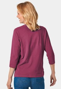 Bordeauxfarbendes T-Shirt mit drei Viertelärmeln, runden Ausschnitt und lässiger Passform. Weicher, glatter Stoff; der Stoff wirkt leicht und angenehm zu tragen.