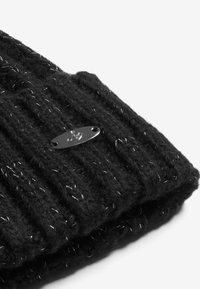 Mustra musta kootud beanie vertikaalsete soontega, mille sisse on keeratud metallilised hõbedased niidid ning millel on väike hõbedane logoplaat.