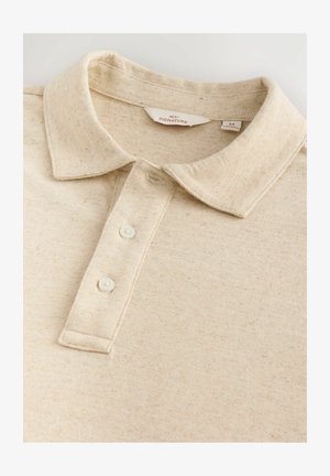 Bež polo majica z teksturirano tkanino, klasičnim ovratnikom, tremi gumbi in diskretnimi madeži po materialu.
