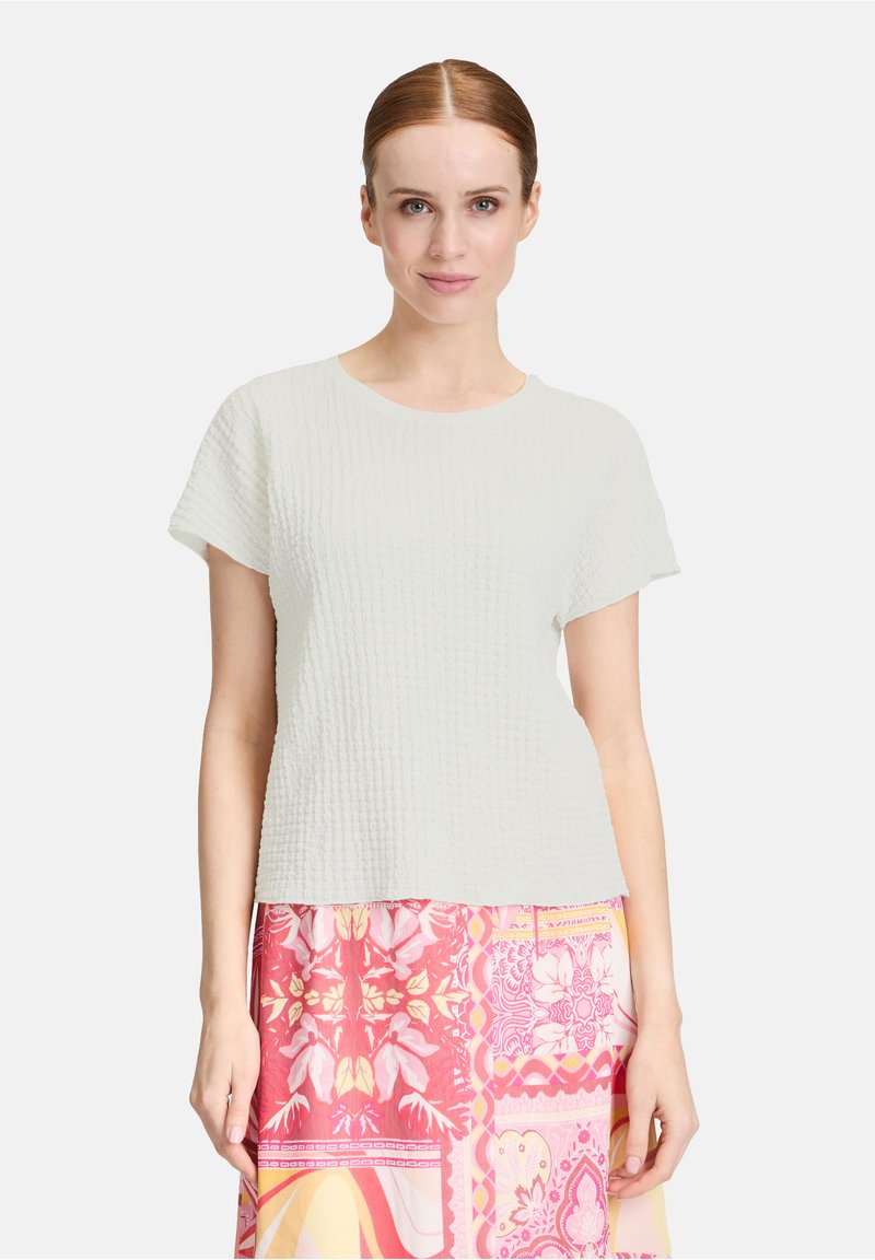 Haut court à manches courtes texturé gris clair avec un col rond ; associé à une jupe à motifs colorés avec des designs roses, jaunes et floraux.