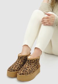 Bruine en tan luipaardprint enkelboots met een dikke platformzool en een zachte, fuzzy voering, gecombineerd met witte versleten jeans.