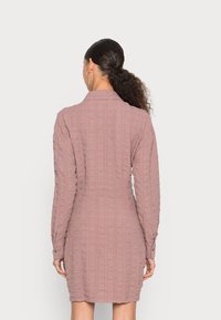 Vestido rosa poeirento com um padrão texturizado em riscas, mangas longas, gola e fecho de botão nos punhos.