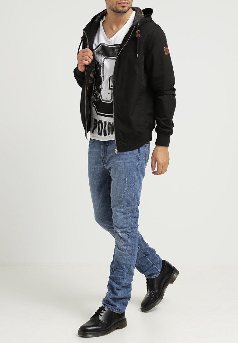 Czarna bluza z kapturem na zamek z troczkami, biały t-shirt z grafiką, niebieskie dopasowane jeansy z przetarciami oraz czarne buty.