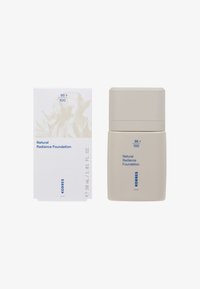 Natural Radiance Foundation i en blød beige flaske. Kvadratisk æske med abstrakt lysmønster. Blå tekst angiver 30 mL, skygge 95 + 100.