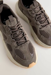 Gray suede and mesh sneakers with a chunky rubber sole, featuring textured accents and padded tongue, laced design, and round toe.