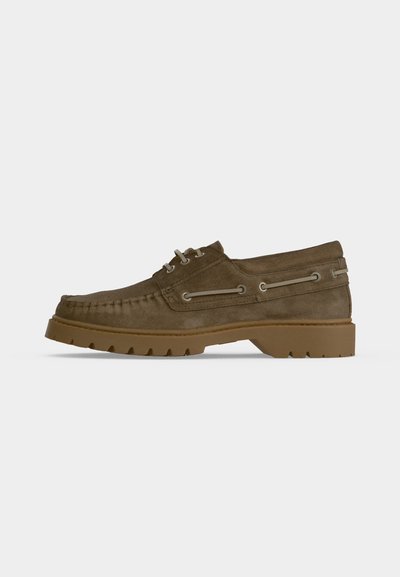 Mocasín marrón de piel de ante con cordones, suela gruesa de goma con tacos y cordones decorativos de cuero en los lados.