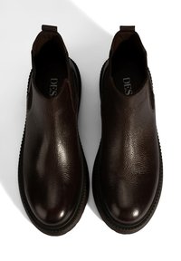 Bruine leren instappers met een textuur, ronde neus, elastische zijpanelen en contrasterende zwarte rubberen zolen.