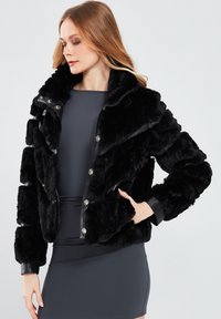 Black faux fur jacket with a cropped design, featuring a high collar, press-stud closure, and leather accents on cuffs and hem.
