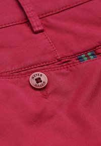 Rode stof met een gladde textuur, voorzien van een zichtbare knop met "MEYER" gegraveerd en kleurrijke stikdetails nabij de naad.