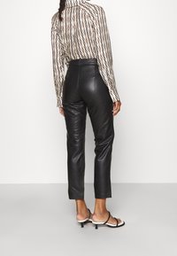 Musta nahkainen korkeavyötäröinen housut slim fit -mallilla, joissa on sileä texture ja hienovarainen kiilto. Yhdistettynä kuviolliseen pitkähihaiseen puseroon.