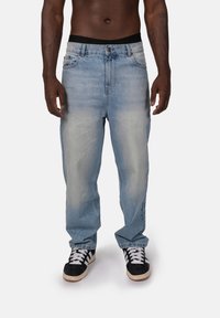 Jasnoniebieskie dżinsy o luźnym kroju, z kieszeniami z przodu, detalami w stylu przetarcia i czarnym pasem, połączone z czarnymi sneakersami.