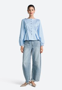 Light blue, long-sleeved peplum blouse with button front, paired with distressed, loose-fit light blue jeans and beige pointed-toe heels.