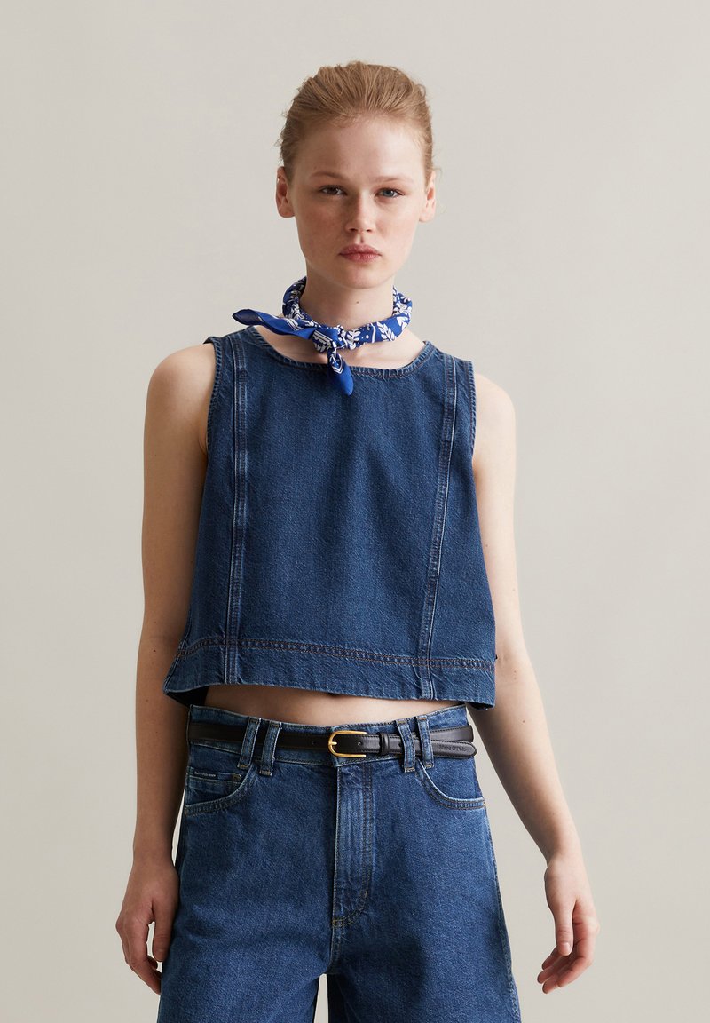 Denimowy crop top z okrągłym dekoltem i bezrękawowym krojem; posiada kontrastowe szwy i lekko postrzępiony dół. Połączony z dżinsami o wysokim stanie.