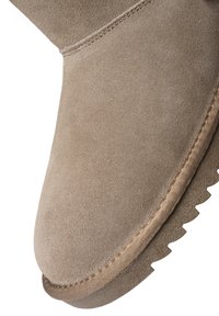 Nahaufnahme einer beigefarbenen Wildlederstiefelspitze mit detaillierter Naht und einer strukturierten Kante der Gummisohle.