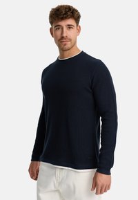 Marineblå vaffelstrikket sweater har en rund hals med hvid trimming, lange ærmer og en ensfarvet kant. Blød tekstur og enkelt design.