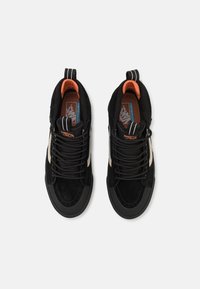 Sorte fløyels høye sneakers med en kremfarget side stripe, sorte lisser og oransje detaljer på innsiden og tungen av skoen.