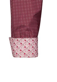 Manschetta di camicia bordeaux con un motivo geometrico. L'interno della manichetta presenta un tessuto bianco con un design floreale rosa. Materiale in cotone testurizzato.