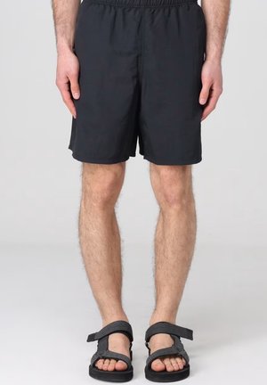 Costumi da bagno neri con vita elasticizzata, realizzati in un tessuto liscio e leggero. Abbinati a sandali scuri con cinturino regolabile.