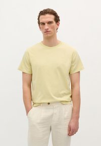 Lys gul bomulds T-shirt med korte ærmer og rund halsudskæring. Båret sammen med beige, plisserede linnedbukser. Enkel design, ingen mønstre.
