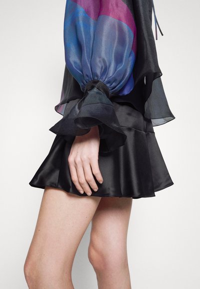 Mini-jupe en satin noir avec un ourlet évasé, assortie d'un blouse colorée en transparence avec des manches volumineuses et un poignet à cordon.