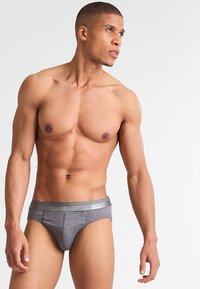 Boxer grigi con una superficie liscia, dotati di un elastico con logo in vita. Il design è aderente e minimalista.