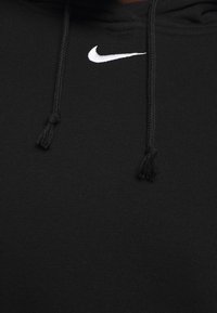 Svart hoodie i mjukt material med en vit Nike-logotyp på bröstet, snoddar med tofsar och en slät yta.