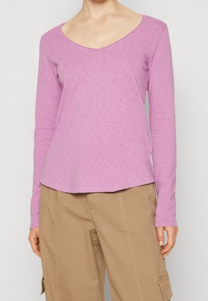 Maglietta a maniche lunghe con scollatura a V in tessuto rosa chiaro, caratterizzata da una vestibilità rilassata e un orlo leggermente curvo, abbinata a pantaloni cargo beige.