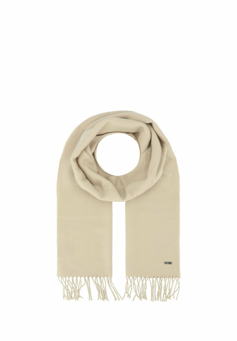 Écharpe beige en matériau doux avec un design circulaire, présentant des bords frangés et une petite étiquette de logo sur un côté.