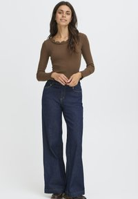 Brun langærmet top med bølgekant ved halsen, parret med vide mørkeblå denim jeans. Begge dele har en glat overflade og klassisk design.