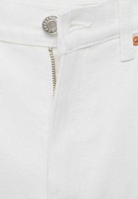 Jean en denim blanc avec fermeture éclair métallique partiellement ouverte et bouton argenté.