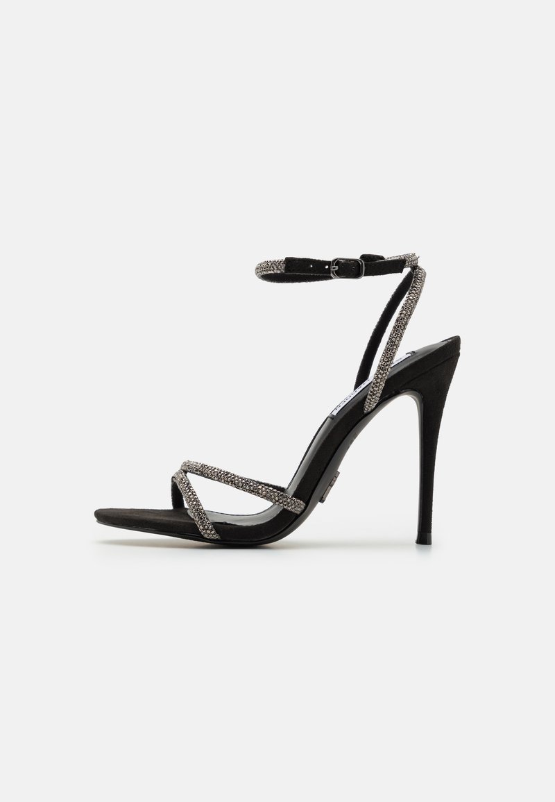 Black high-heeled sandal with thin, bejeweled straps and an ankle buckle. Suede material, open toe, and a sleek, pointed silhouette.