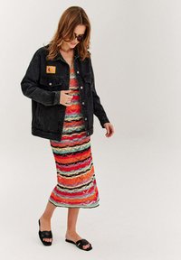 Czarna kurtka dżinsowa z żółtą naszywką. Kolorowa, wzorzysta sukienka dzianinowa w poziome paski w kolorach czerwonym, różowym, niebieskim i kremowym. Czarne sandały.