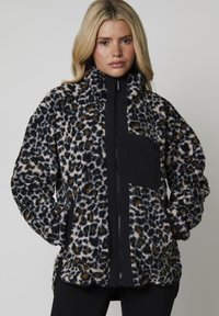 Fleecejacka med leopardmönster, svart dragkedja fram och bröstficka. Mjuk, texturerad tyg med hög krage och sidofickor.