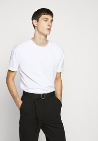 White cotton T-shirt with short sleeves and a crew neck, paired with black trousers featuring a belt. Simple and casual design.